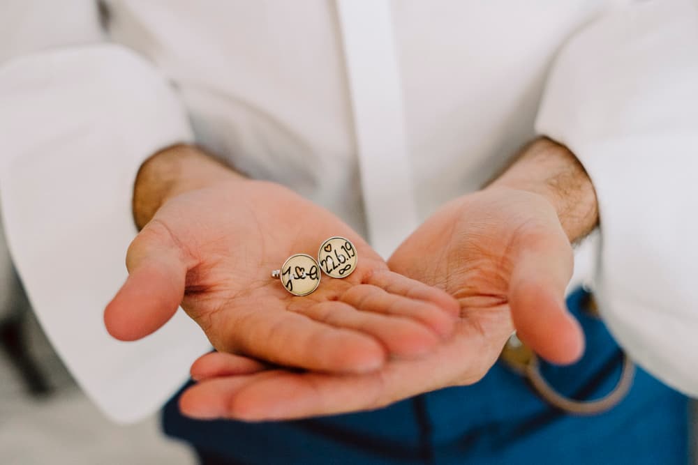 Groom showing his handmade suit buttons with the initials of the wedding couple and their wedding date