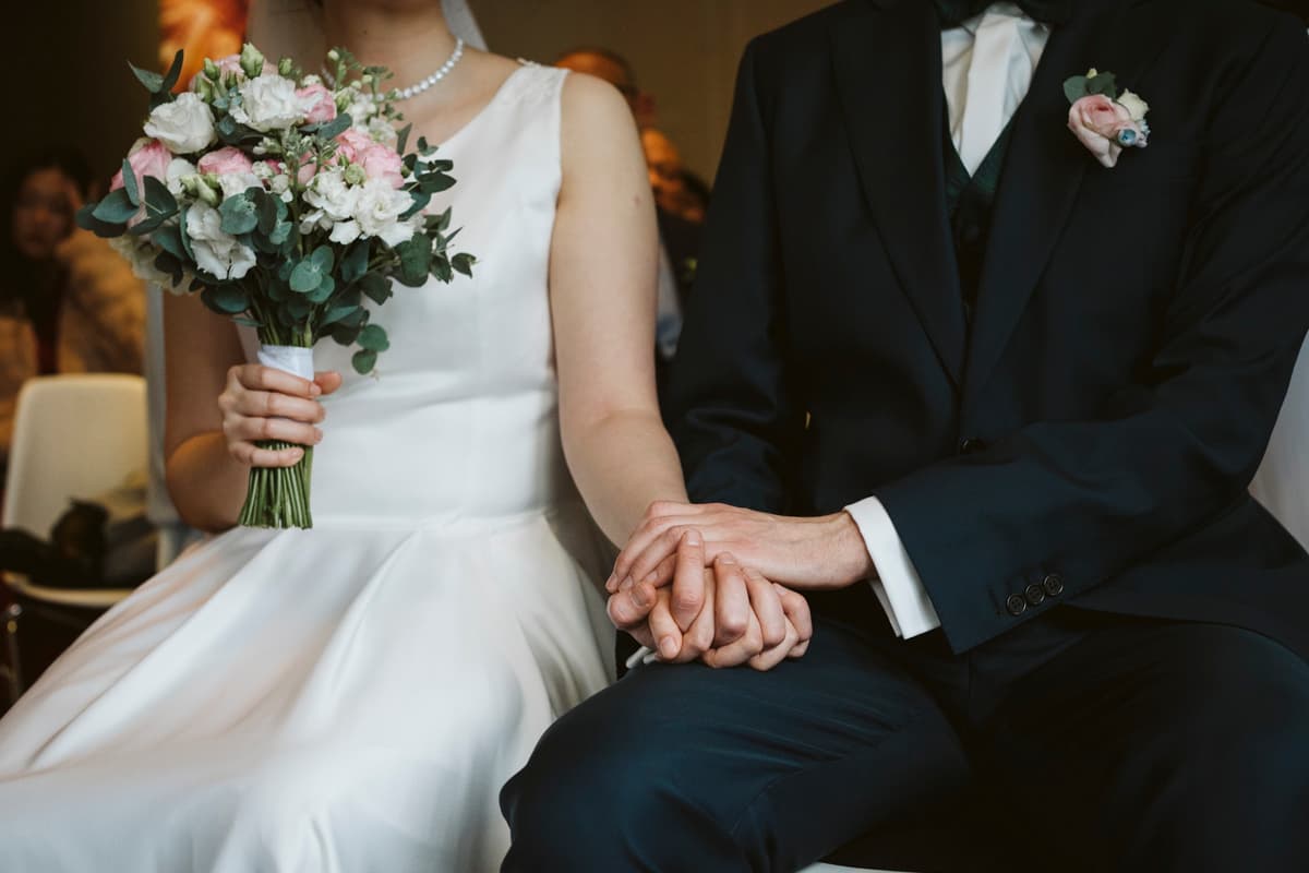 The wedding couple holding hands and a flower bouquet during the wedding ceremony at Gästehaus Blumenfisch in Berlin Wannsee